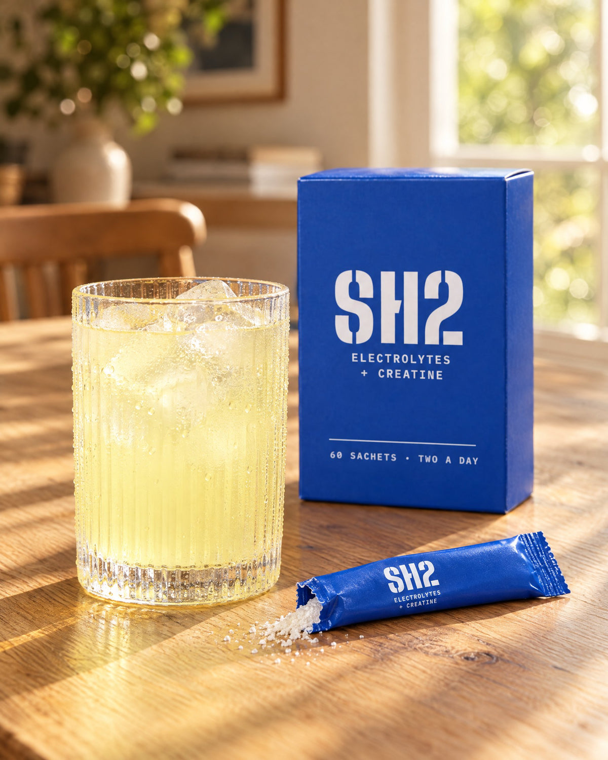 Glass of SH2 with ice next to the box and an open sachet
